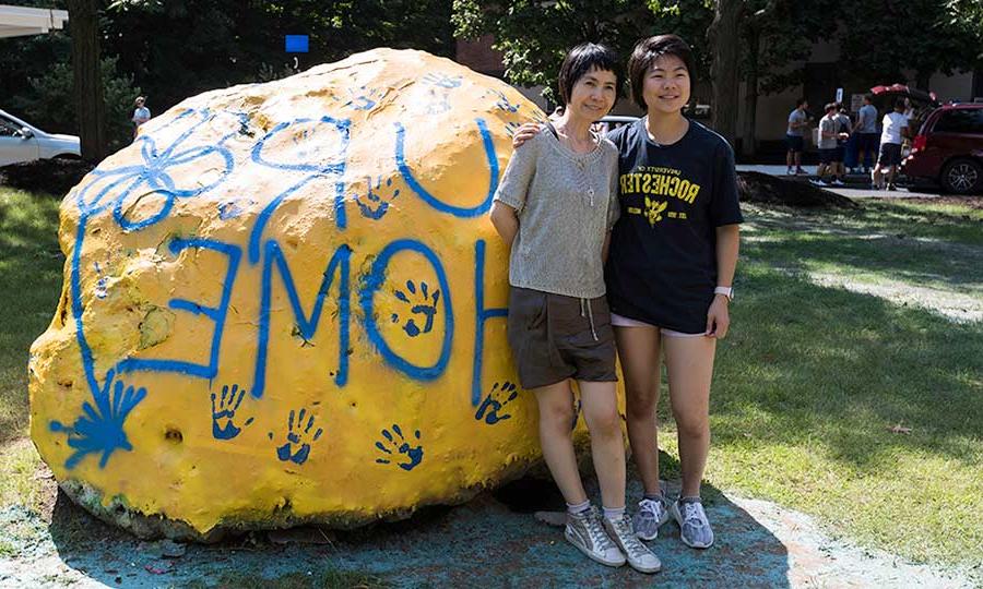 mother and daughter standing outside of residence hall in front of a large rock painted to read UR HOME